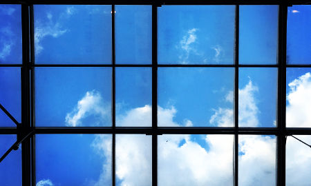 Okno, przez które widać błękitne niebo i delikatne białe chmurki