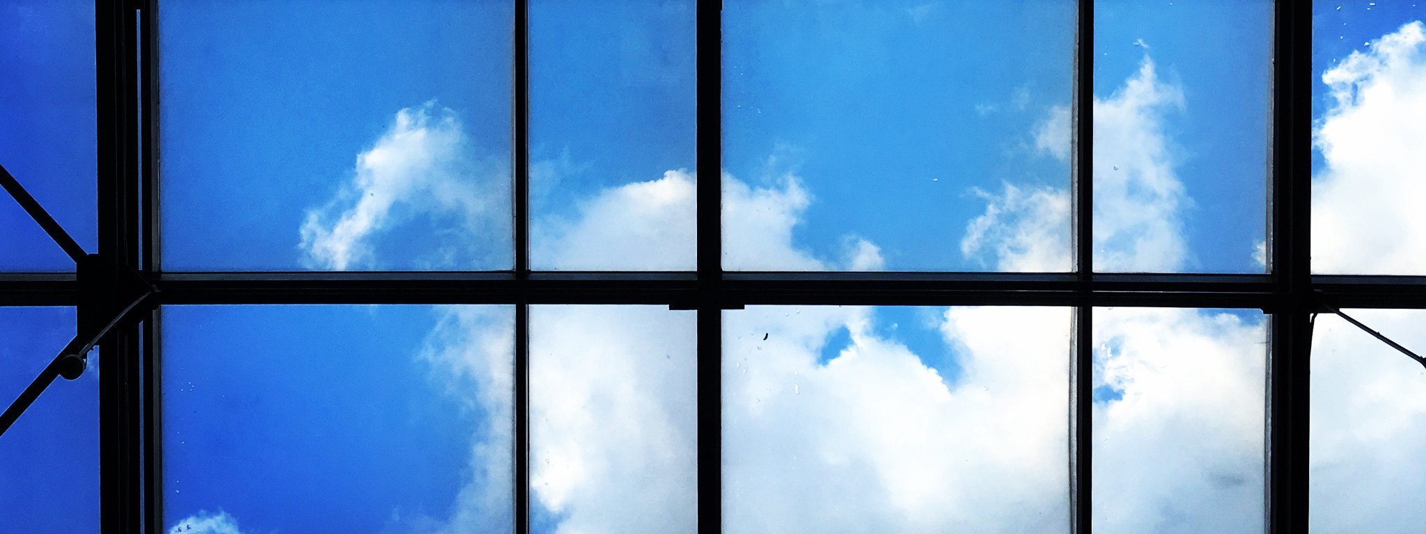 Okno, przez które widać błękitne niebo i delikatne białe chmurki